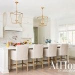 White kitchen with marble backsplash, island with bar stools, and gold lantern pendant lights.