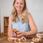 Woman holding wooden toy with beaded toys on table. "AtHome in Arkansas" logo.