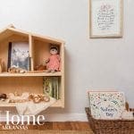 Wooden house-shaped shelf with books, toys, and a doll.