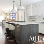 Kitchen with dark gray island, white marble countertop, white cabinets, and pendant lights.