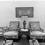 Two armchairs with patterned upholstery flank a dark side table with a lamp.