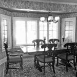 Dining room with dark wood table, chairs, patterned wallpaper, and bay windows.