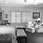 Bedroom with large bed, upholstered chairs, and a lighthouse painting.