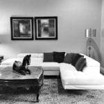 White sectional sofa with dark pillows on a patterned rug, marble coffee table with horse sculpture.