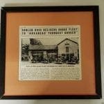 Framed newspaper clipping with headline "SADLEN-ROSS DELIVERS DODGE FLEET TO 'ARKANSAS' YOUNGEST