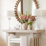 Entryway console table with wood frame, white lamps, and floral arrangements.