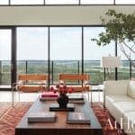 Living room with white leather sofa, two tan chairs, wooden coffee table, and large windows with