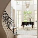 White curved staircase leads to a grand foyer with a piano and chandelier.