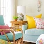 Light blue sofa with yellow and pink pillows, a table with a lamp and plant, and a decorative wall