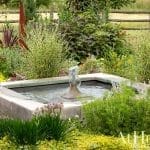 Stone fountain and flower garden with a wooden fence.