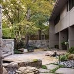 Stone patio with boulders, trees, and a modern building.