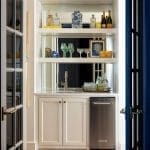 White and blue built-in bar cabinet with glassware and books.
