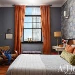Bedroom with patterned wallpaper, orange curtains, and a bed.