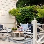 White picket fence with Adirondack chairs and a blue rug.
