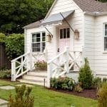 White cottage with pink front door and porch details.