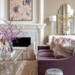 Abstract painting above a marble fireplace with a purple sofa and decorative pillows.