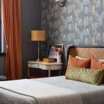 Gray bedroom with patterned wallpaper, orange accents, and a bedside table.