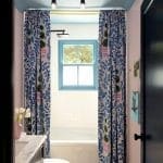 Blue and white tiled bathroom with a patterned curtain and a black chandelier.