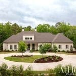 Two-story house with gray roof and white facade, surrounded by trees and landscaping.