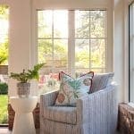 White armchair with striped pillow near window, fern plant.