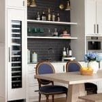 White kitchen bar with dark brick backsplash, wine refrigerator, and seating.