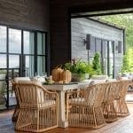 Outdoor dining table with rattan chairs, large windows, and wood siding.