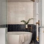 Modern bathroom with a white soaking tub, navy tile, and brass fixtures.