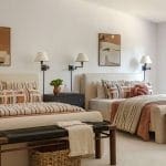 Double bed in a beige room with wall-mounted lamps and artwork.