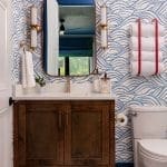 Powder room with blue wave wallpaper, brass sconces, and a wood vanity.