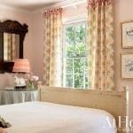 Pink bedroom with floral curtains, mirror, and window.