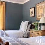 Blue bedroom with twin beds, yellow curtains, and framed prints.