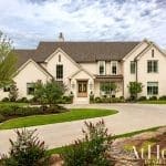 Two-story beige house with a gray roof, landscaping, and driveway.