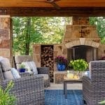 Stone outdoor patio with seating, firewood, and a blue vase.