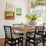 White dining room with lemon artwork, wicker chairs, and a patterned window shade.