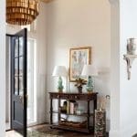 Gold-trimmed ceiling fixture, dark door, and console table with lamps.