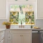 White kitchen with yellow and green patterned curtains, window view, and a copper sink.