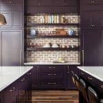 Dark purple kitchen cabinetry with brick backsplash and shelves.