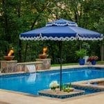 Blue umbrella over a pool with a waterfall and fire pits.