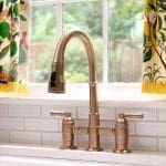 Brass faucet and sink with yellow and floral curtains.