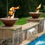 Two fire bowls with flames flank a stone fountain.
