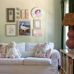 White sofa with floral pillows, framed artwork, and a lamp.