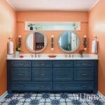Blue vanity with double sinks, marble countertop, and patterned tile floor.