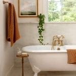 White marble bathroom with a gold faucet, bathtub, and woven towel.