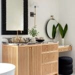 Wooden vanity with marble countertop, gold fixtures, and a black-framed mirror.
