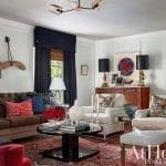 Living room with velvet sofa, patterned rug, and dark drapery.