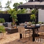 Outdoor dining area with black umbrella, plants, and a wooden fence.