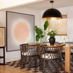 Dining area with a large abstract painting, rattan chair, and a woven rug.