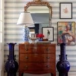 Dark wood dresser with mirror and artwork in striped wallpaper room.