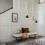 White paneled entryway with bench, bookshelf, and staircase.