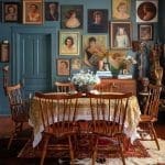 Dark teal wall with framed portraits and a wooden dining table.